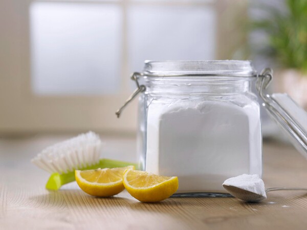 Close-up de recipiente com bicarbonato de sódio, limão cortado ao meio e escova sobre superfície de madeira.