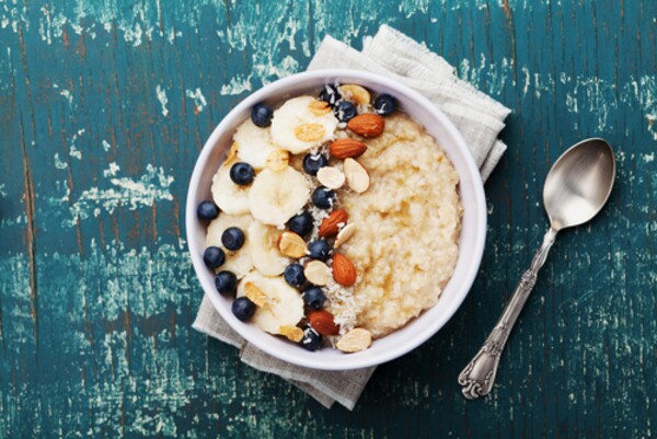 Tigela de aveia cremosa servida com banana fatiada, mirtilos, amêndoas, lascas de coco e calda de caramelo 