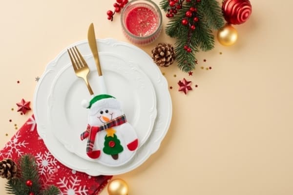 Ambiente festivo de Natal criado por mesa posta com guardanapos vermelhos, enfeites dourados e verdes, velas acesas e louças brancas alinhadas para a ceia.