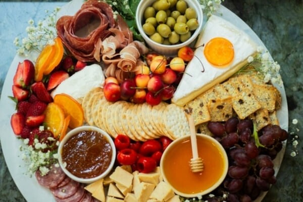 Tábua de frios com carnes curadas, queijos variados, frutas frescas e acompanhamentos, dispostos de forma apetitosa sobre uma superfície rústica.