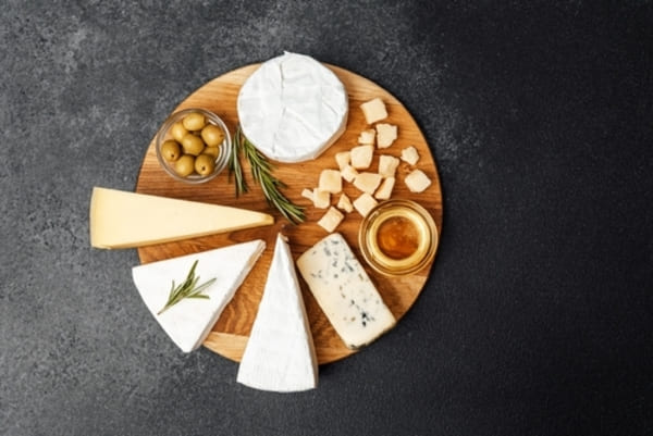 Tábua de madeira com uma seleção de queijos variados, acompanhada por azeitonas, disposta sobre uma superfície escura.