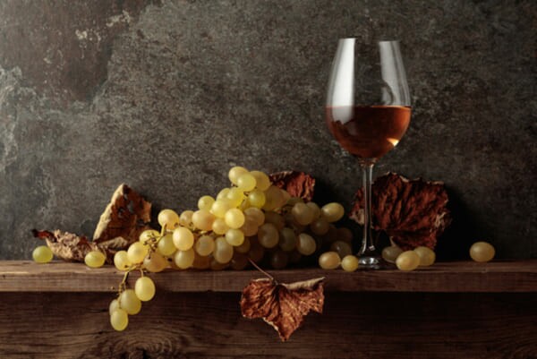 Taça de vinho branco ao lado de uvas frescas e ramos secos de videira sobre uma superfície rústica, com iluminação suave que evoca o clima outonal.