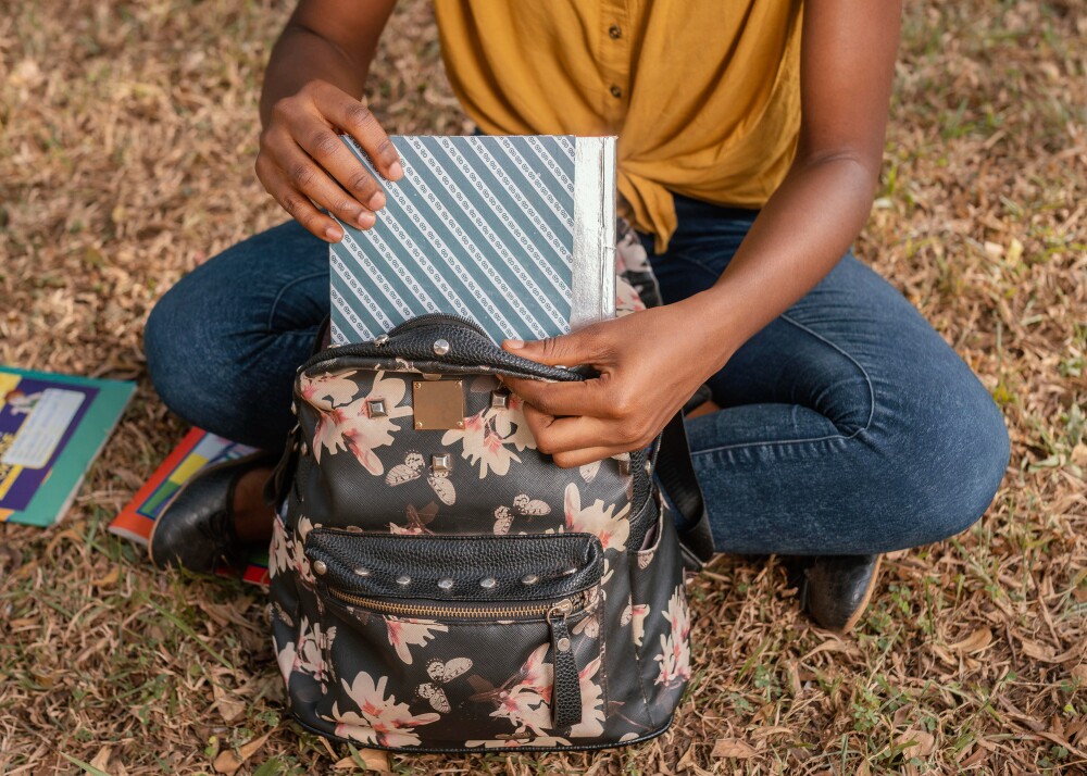 Estudante retirando um caderno de dentro da mochila escolar. 